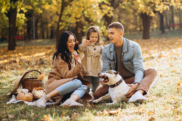 Fototapeta premium Portrait of happy young family sitting on blanket together and playing with dog in autumn park