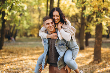 Happy couple, man holding a woman behind his back and having fun together in the autumn park