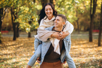 Happy couple, man holding a woman behind his back and having fun together in the autumn park