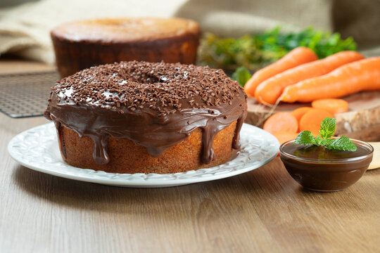 Brazilian carrot cake with chocolate frosting on wooden table with carrots in the background