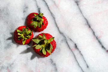 Obraz na płótnie Canvas Close up of three strawberry tops on marble 