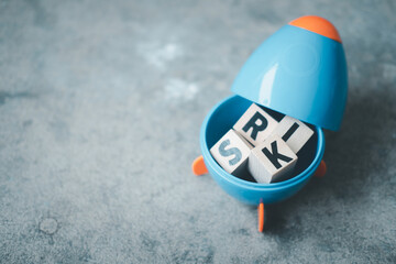 Cube wooden block with alphabet building the word RISK in blue rocket.
