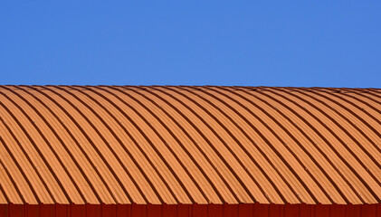 Curve line pattern of orange corrugated steel curved roof against blue clear sky background