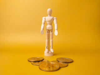 Wooden mannequin stand infront bitcoins on a yellow background.