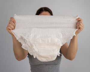 A caucasian woman holds an adult diaper and checks its strength on a white background. 
