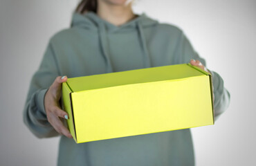 A woman holds a yellow box. On a gray background