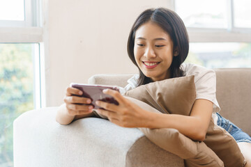 Home lifestyle concept, Young woman sit on couch and hug pillow to play games on smartphone at home