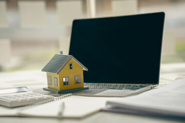 Real estate business idea on a desk with a small house and laptop in the office.