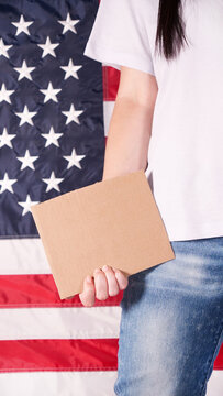Young woman holding blank sign in her hands close up. American flag on background.