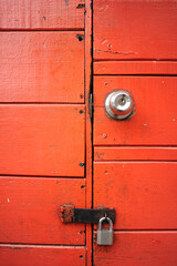 Fototapeta premium Close-up of an old red wooden door with a gray metal padlock.