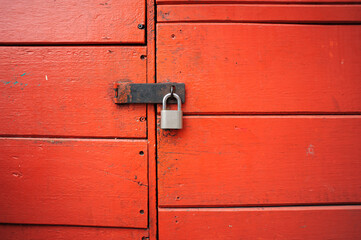Close-up of an old red wooden door with a gray metal padlock.