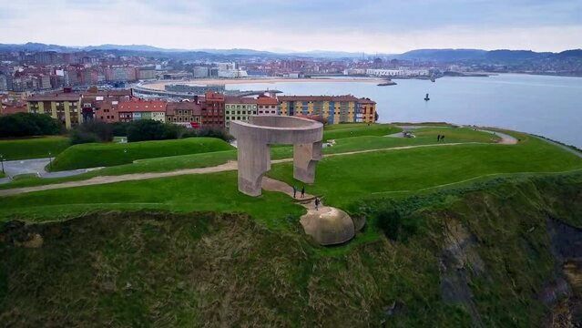 unique revealing drone shoot of 
Elogio del horizonte  scuplture in Cimadevilla in Gijón where we see the bay and the sea and the mountain of the city in the background during a quiet cloudy afternoon