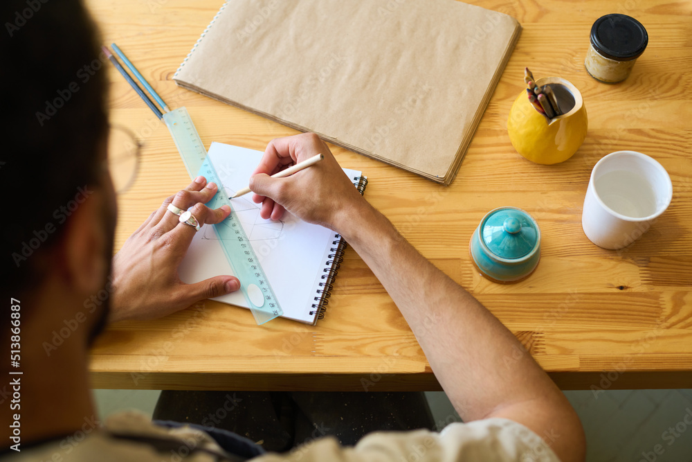 Aufkleber above view of hands of young man with pencil and ruler drawing sketch of new creative earthenware it