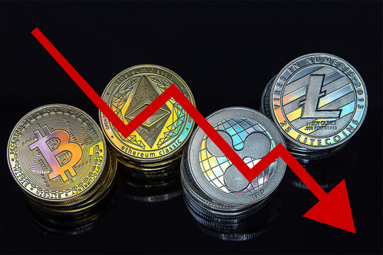 Cryptocurrency tokens, including Bitcoin, Ethererum Ripple, and Litecoin saw from above on a black background. A red arrow goes down, representing the decline in the exchange rate of the coins. 