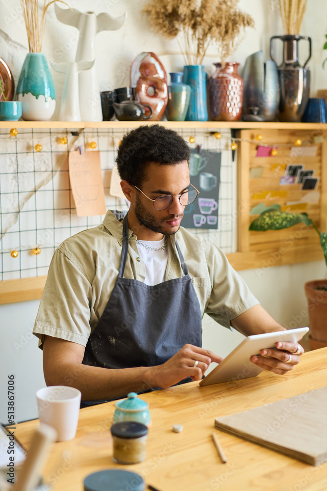 Aufkleber Serious guy in casualwear and apron looking at screen of digital tablet while scrolling through online information and creative ideas