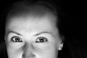Black and white photograph of an attractive woman. A large portrait on a dark background. Macro photo, top of the face. Front view.