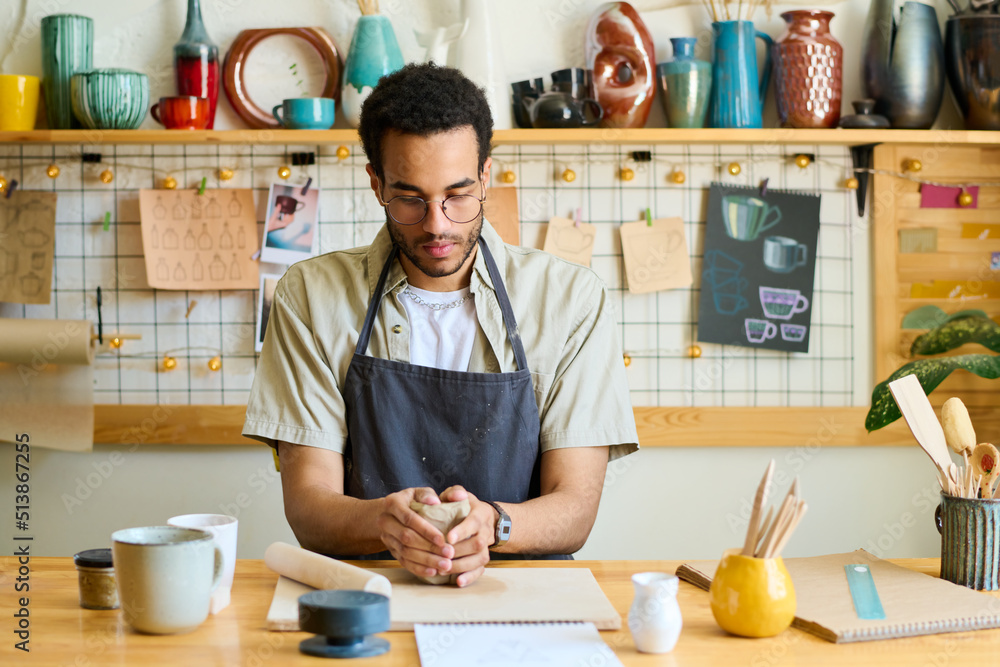 Aufkleber Young creative black man skilled in making earthenware sitting by table in workshop or studio and creating new clay item on board