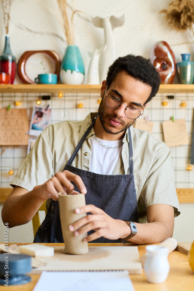 Poster creative male pitcher making new clay vase or jug while sitting by table with supplies for creatibe 