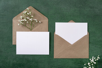 Blank greeting cards and envelopes with gypsophila on green background. Blank paper sheet cards...