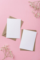 Blank greeting cards and envelopes with gypsophila on pink background. Blank paper sheet cards with mockup copy space. Minimal workplace composition. Flat lay, top view