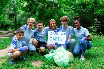 Diverse Group of People Picking Up Trash in The Park Volunteer Community Service. Happy international volunteers holding placard with 'Save the Earth' message.