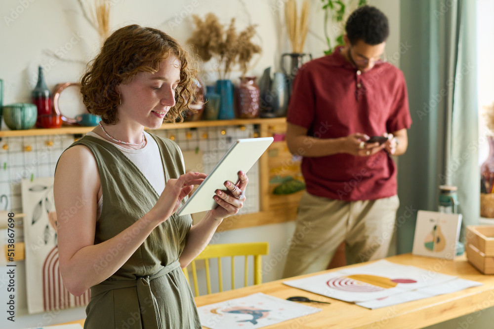 Aufkleber Young interracial coworkers using mobile gadgets while taking photo of drawing and working over new creative project in studio