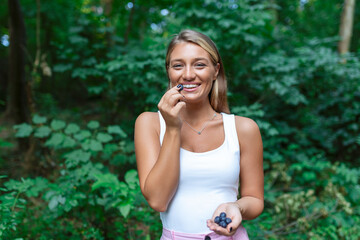 Young happy woman eating blueberries in green summer garden, looking at camera and smiling