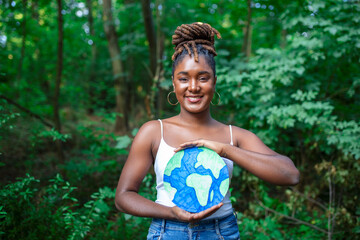 African woman activist holding planet earth poster in woods, environmental pollution concept.