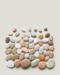 Creative arrangement of natural colored sea stones. Smooth round pebbles as square pattern on beige background. Minimal trend summer flat lay, top view still life composition with rocks