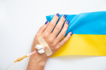Fototapeta premium A woman's hand with a dropper and the flag of Ukraine on a white background, the war in Ukraine, civilians are killed in the war 2022