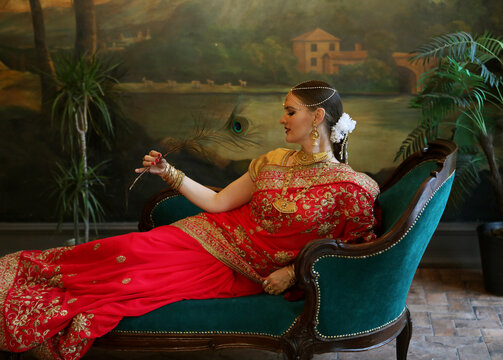 A charming young woman is holding a peacock feather while sitting on a sofa.