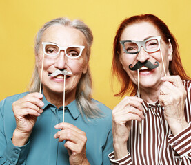 funny elderly female friends with fake mustache and glasses, laughs and prepares for party over...