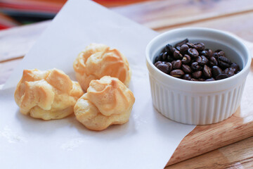 Eclairs on white paper and coffee beans in white cup.Eclair pastry with white paper Placed on a wooden tray.