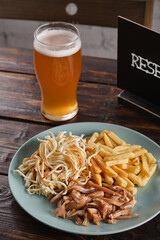 Appetizer for beer. Assorted smoked meat, salted cheese and French fries in a plate on a wooden table. Vertical orientation, copy space, no people