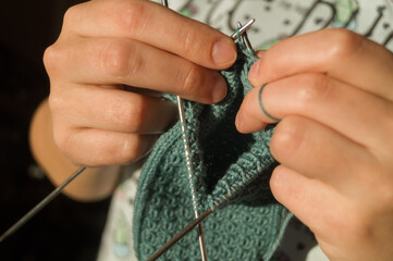 Close-up hand knitting. Hobbies, handicrafts. Knitting warm clothes from woolen fine yarn by hand on metal needles. Selective focus
