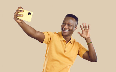 Cheerful African American man taking selfie on mobile phone. Happy Tanzanian guy waving hello and...