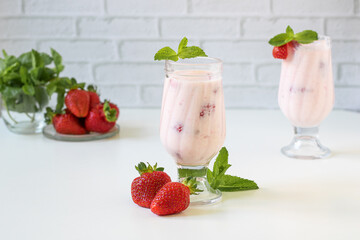 Milkshake in glasses decorated with mint. Strawberries are nearby.