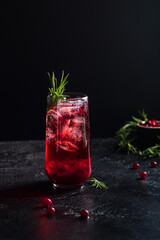 Iced cranberry drink garnished with rosemary. Near sprigs of rosemary and cranberries.