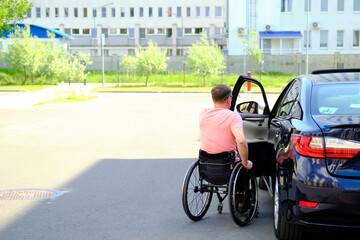a man in a wheelchair closes the door of his car, driver with disability
