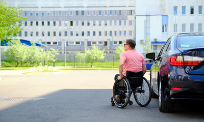 a man in a wheelchair next to a dark blue car, copy space, driver with disability