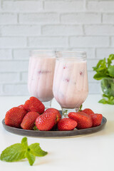 Strawberry milkshake. Two glasses of cocktail on a platter with strawberries, mint next to it.