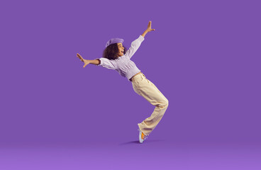 Cheerful joyful african american teenage girl having fun getting on her toes on purple background....