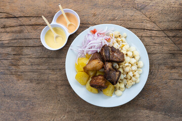Peruvian food: Chicharron with potatoes, white corn and onion served on a rustic wooden table. fried pork meat with potatoes and onion. Top view