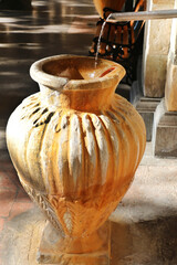 An old large clay jug into which flows a stream of water from a tap, close up