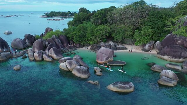 Belitung, Indonesia - June 25 2022: Aerial drone footage of people visiting and doing stand up paddle in the stunning Tanjung Tinggi beach in Belitung, famous for its rocks