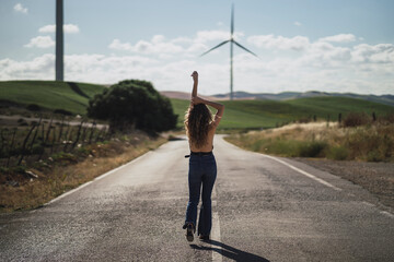Chica joven delgada delante de campo eolico y posando en la carretera