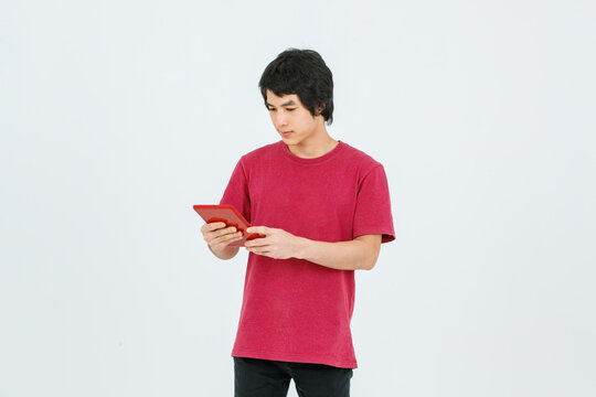 Portrait isolated cutout studio shot of Asian young handsome teenager male model in street style outfit standing holding tablet computer in hands smiling taking selfie photo on white background