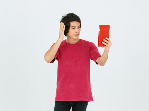 Portrait isolated cutout studio shot of Asian young handsome teenager male model in street style outfit standing holding tablet computer in hands smiling taking selfie photo on white background