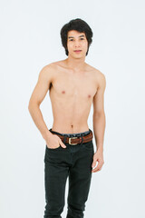 Fototapeta premium Portrait isolated cutout studio shot of Asian young handsome confident slim thin muscular shirtless teenager male model standing posing holding hand in denim jeans pants pocket on white background