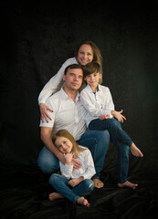 portrait of happy family with two kids in white shirts and blue jeans in studio on black background